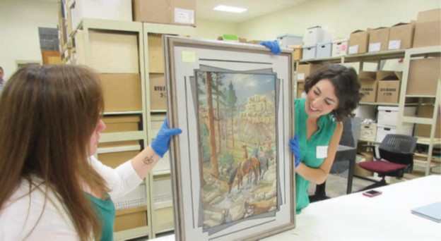 An image of two women looking at a painting with gloves on.