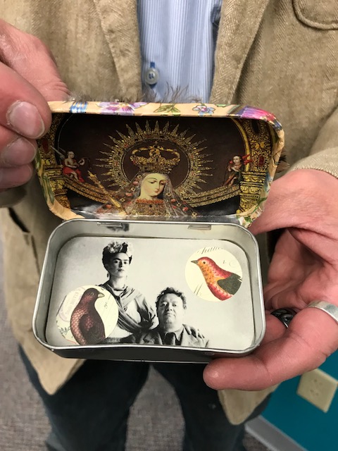 An image of a person holing a small tin box with images of people inside.