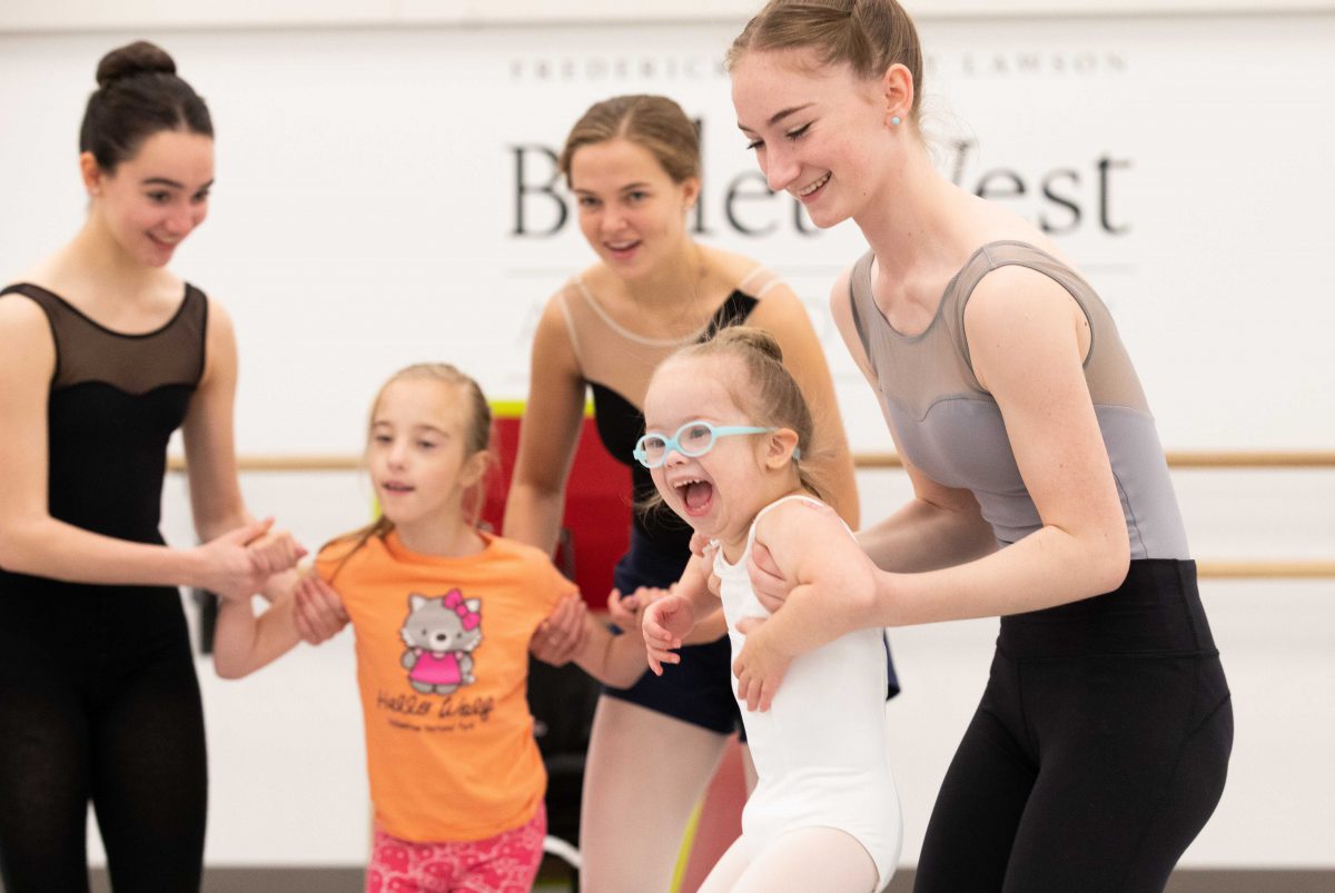 A photo of three teenage ballerinas with two younger girls.