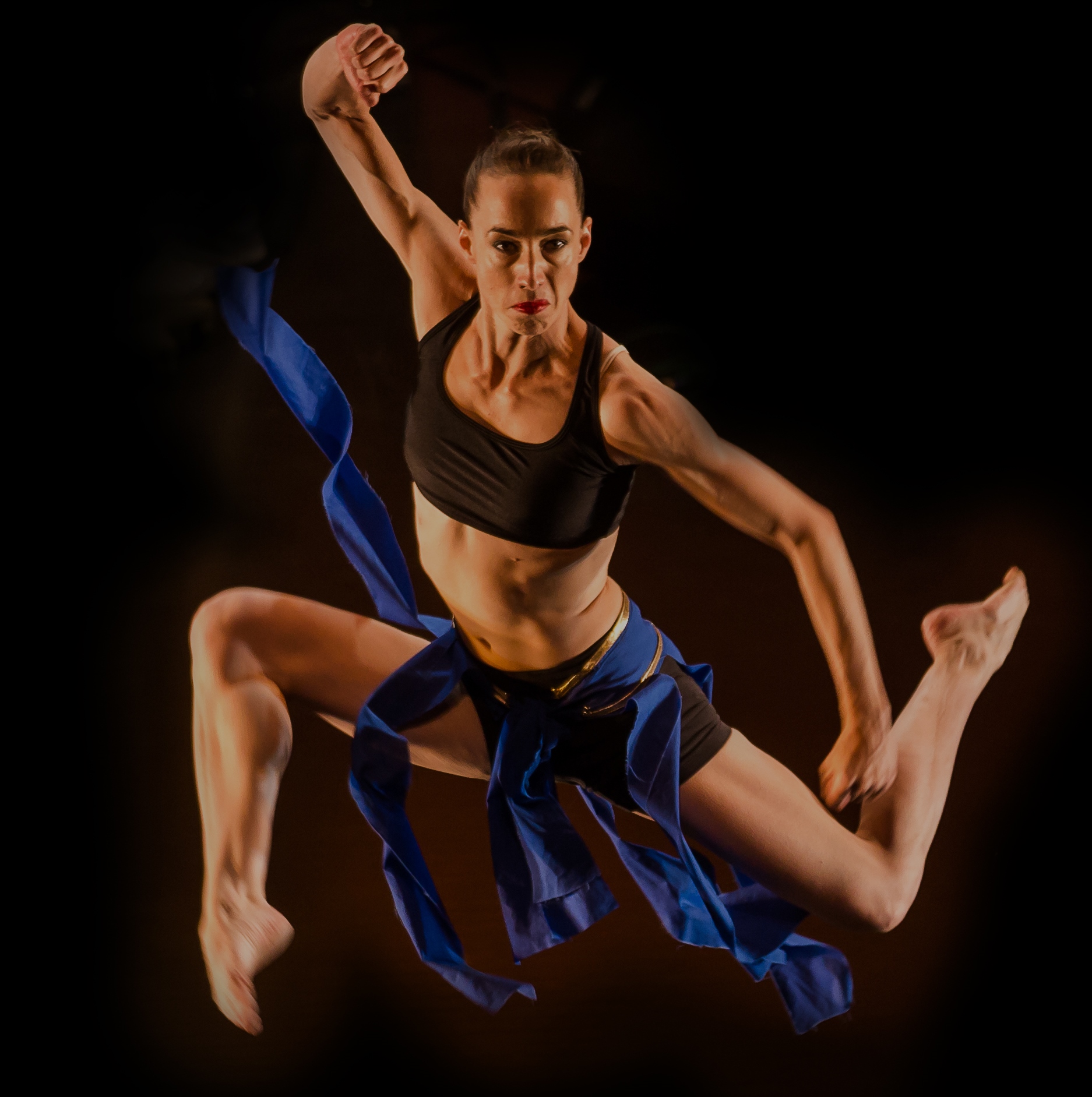 A photo of a white woman wearing blue strips of fabric, dancing.