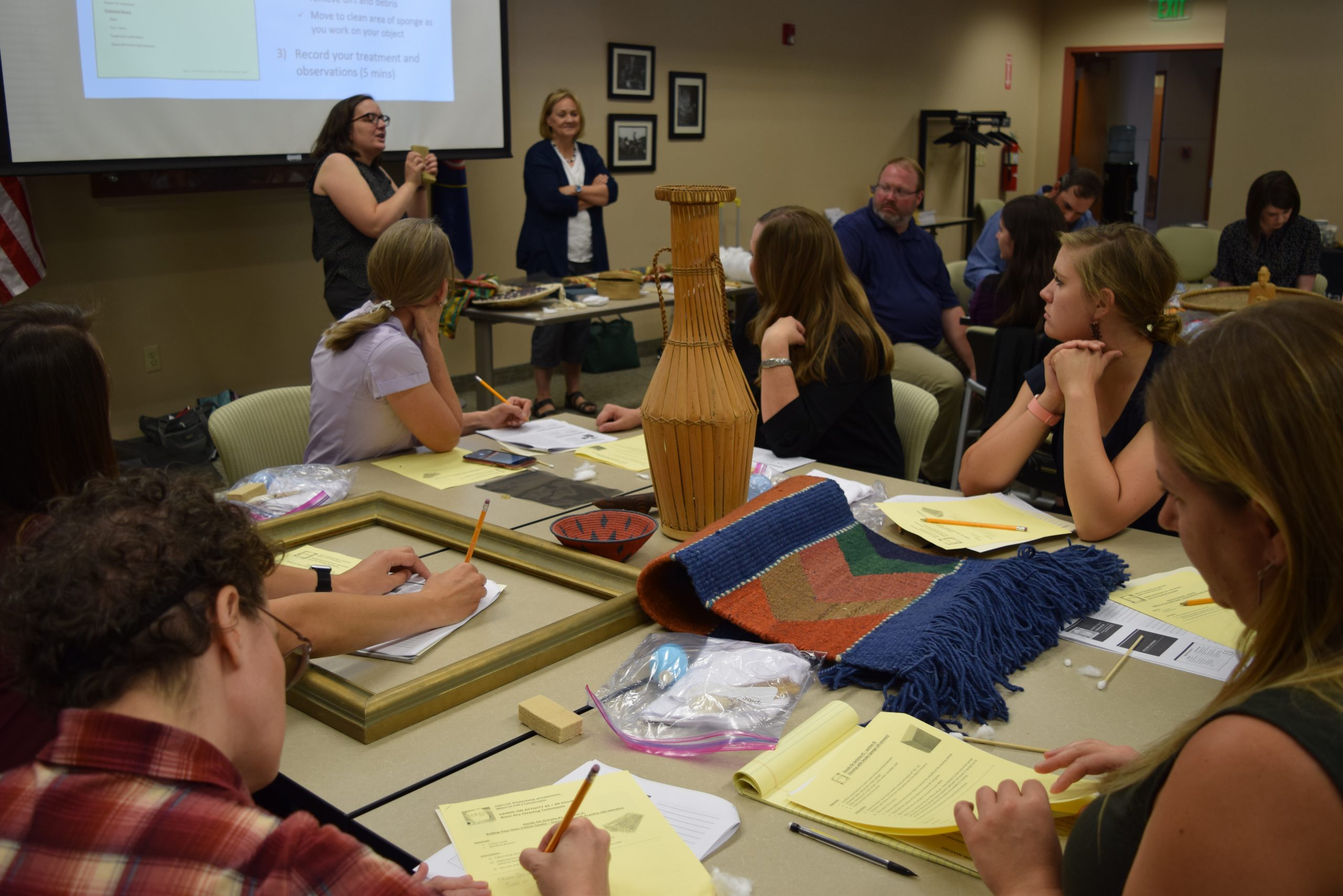 People sit at tables in a classroom setting while watching a presenter.