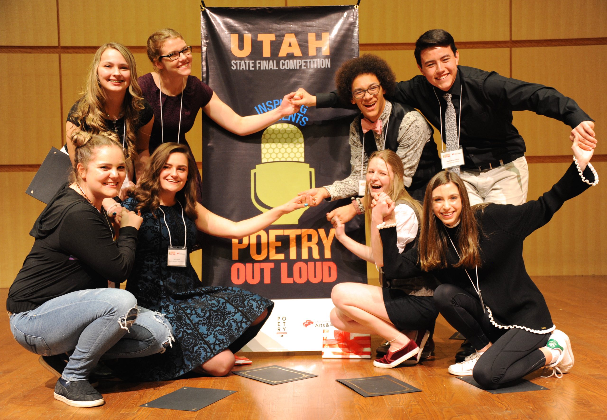 A group of students gather around a sign for Poetry Out Loud.