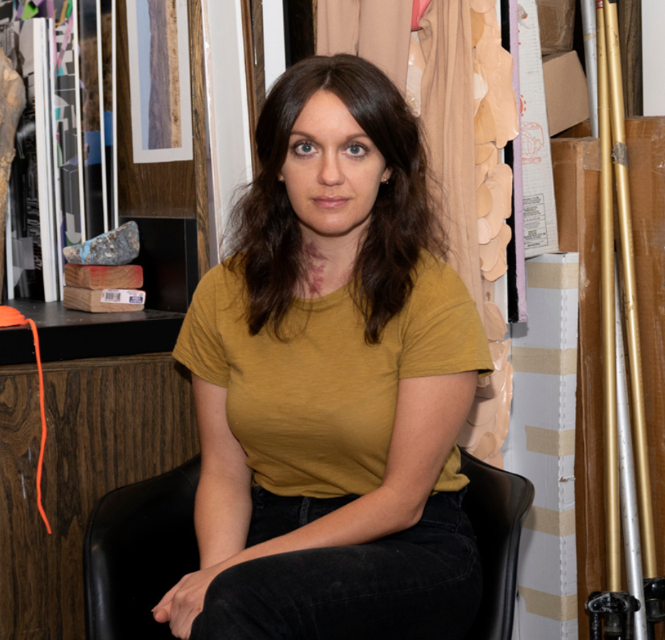 A woman with long dark hair poses in her art studio.