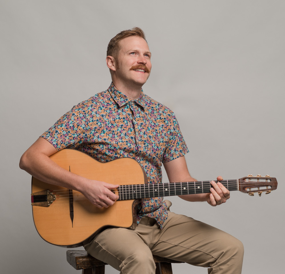 A man with a mustache plays an acoustic guitar.