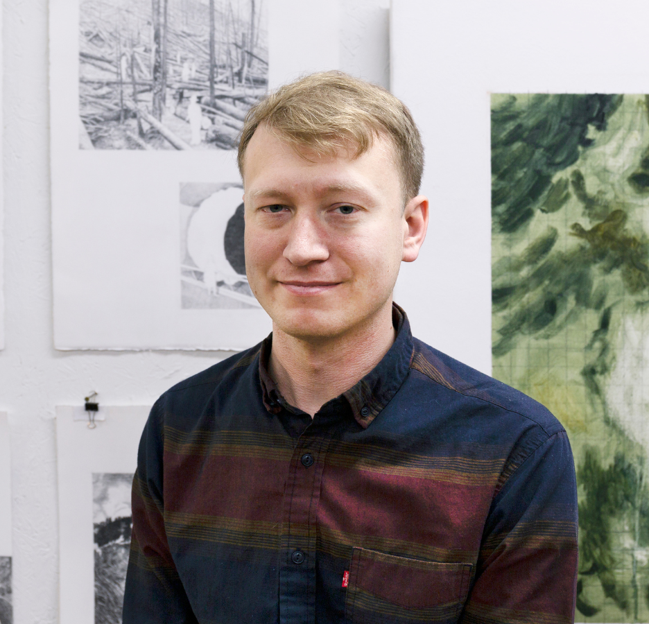 A blond man poses in front of his artwork.