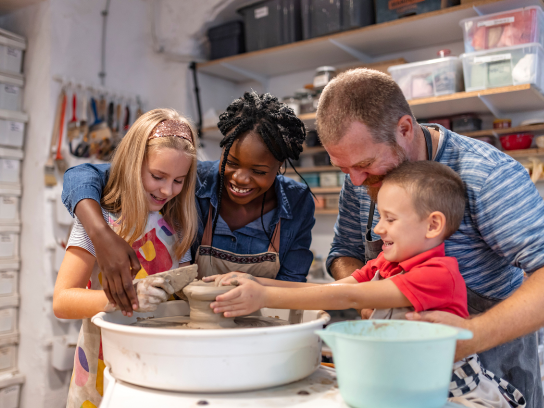 Two adults and two children make a clay pot together.