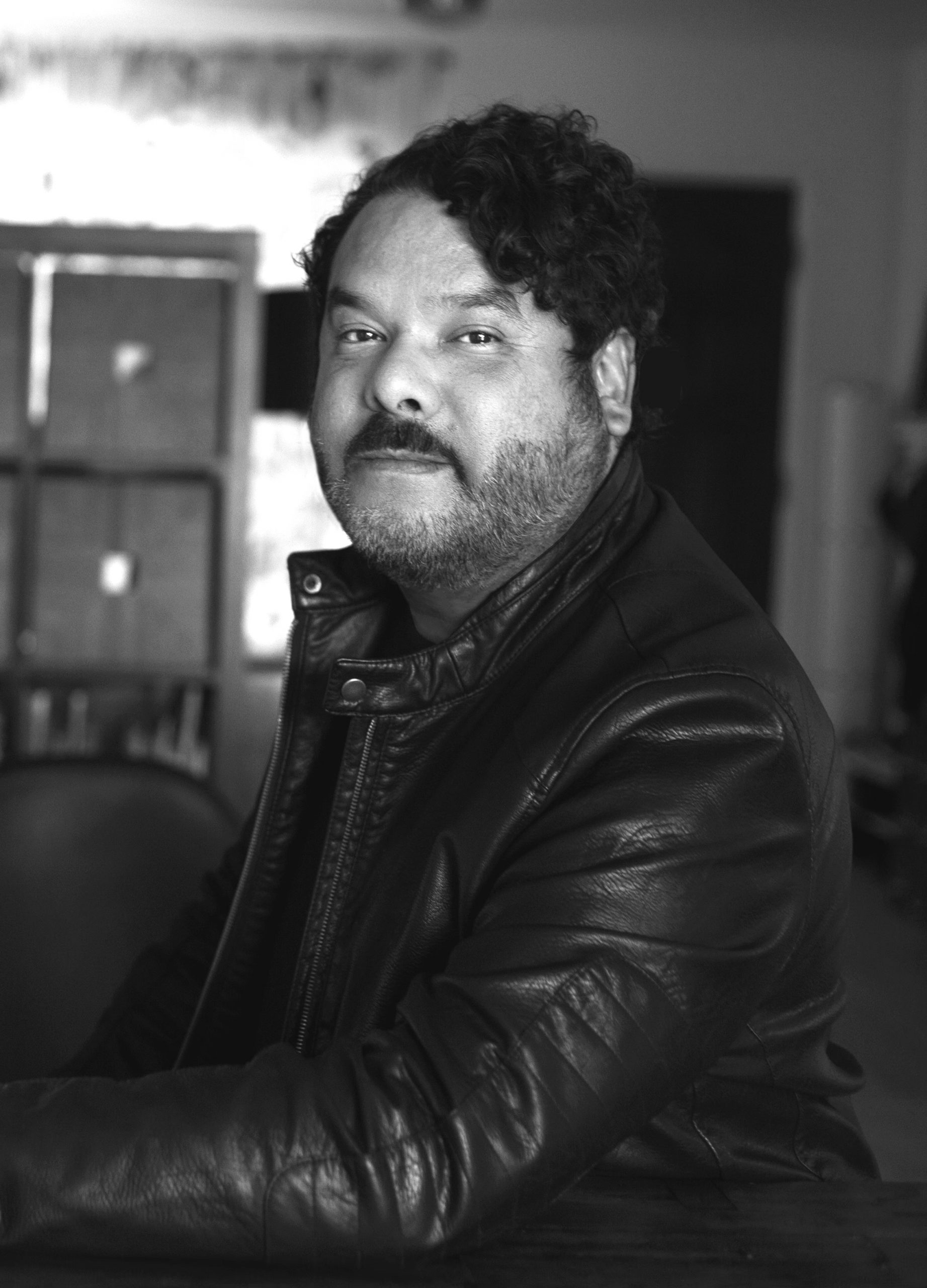 A man with short, dark, curly hair looks at the camera.