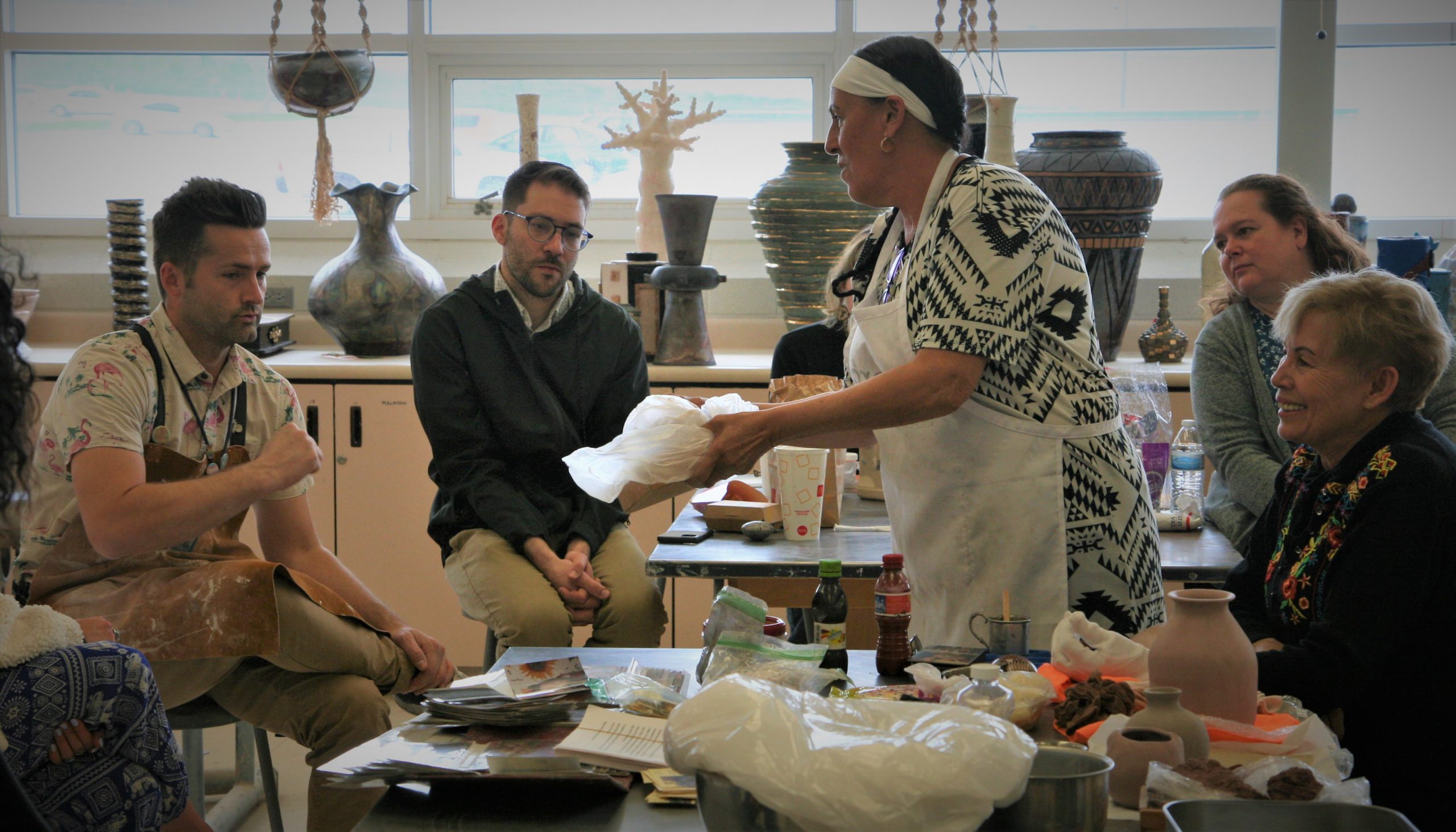 Four individuals sitting around an instructor in a pottery workshop.