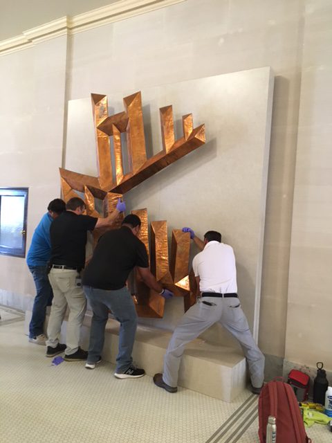 People hang a copper sculpture on a marble wall.