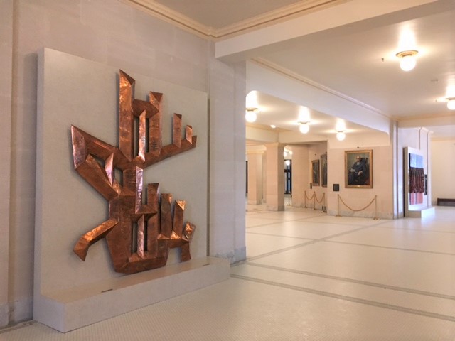 An abstract copper sculpture in a marble hallway.