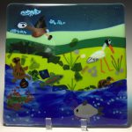 Glass art featuring animals and birds near running water and greenery.