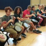 Young students sitting and playing a drum held in their lap.