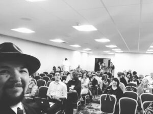 a black and white photo of author Jared Quan in a crowded hotel convention room