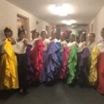 Ten dancers in flowing, brightly colored skirts pose for a picture