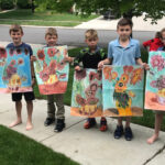 Several elementary students holding chalk drawings of colorful flowers