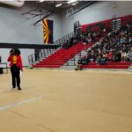 Yemisi Agbebi speaking in a school gymnasium to a large assembly of students