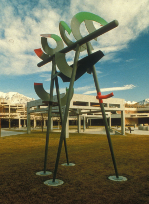 An abstract outdoor metal sculpture in gray, green, and red.