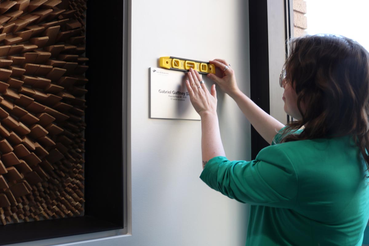 A woman using a level to hang a sign on the wall.