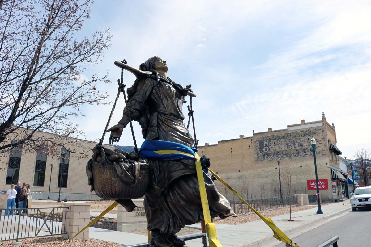 A bronze statue of a woman with two large baskets of fruit.