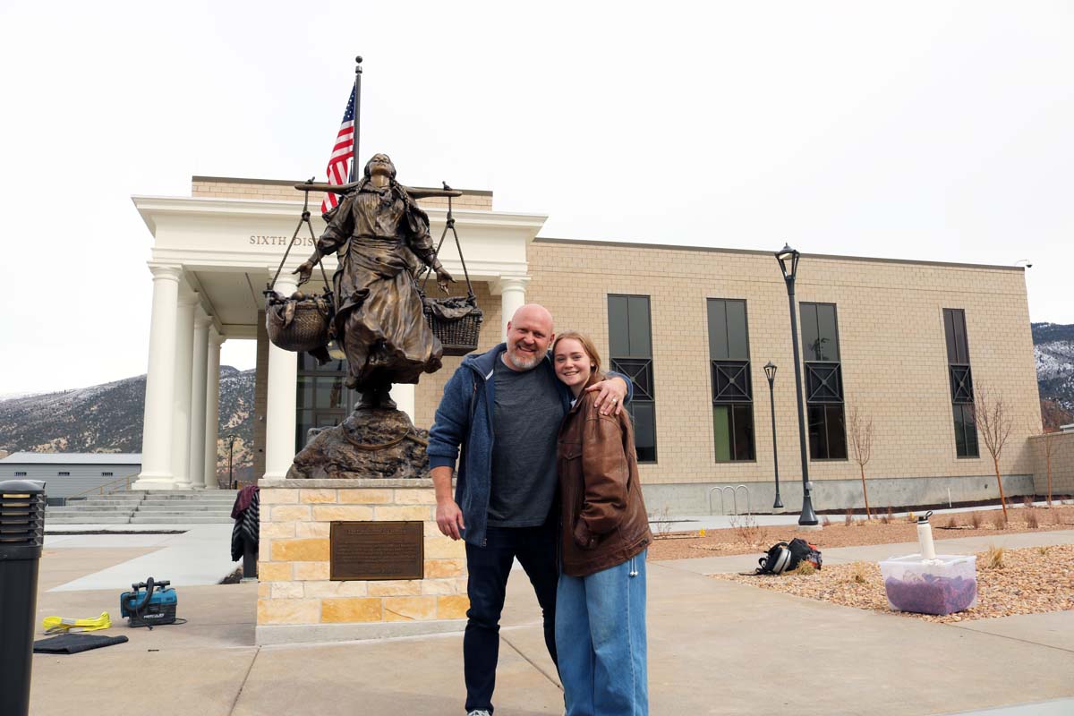 A man and his daughter in front of a large bronze statue.