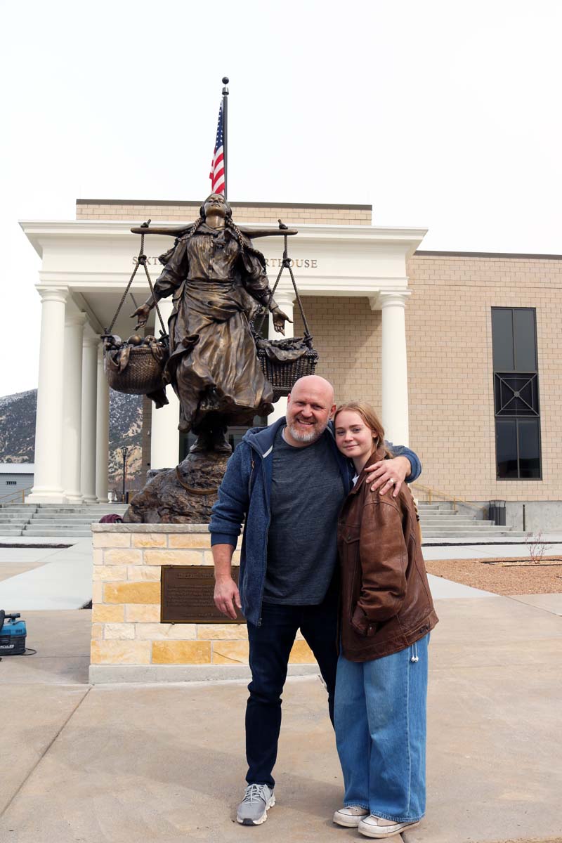 A man and his daughter in front of a large bronze statue.