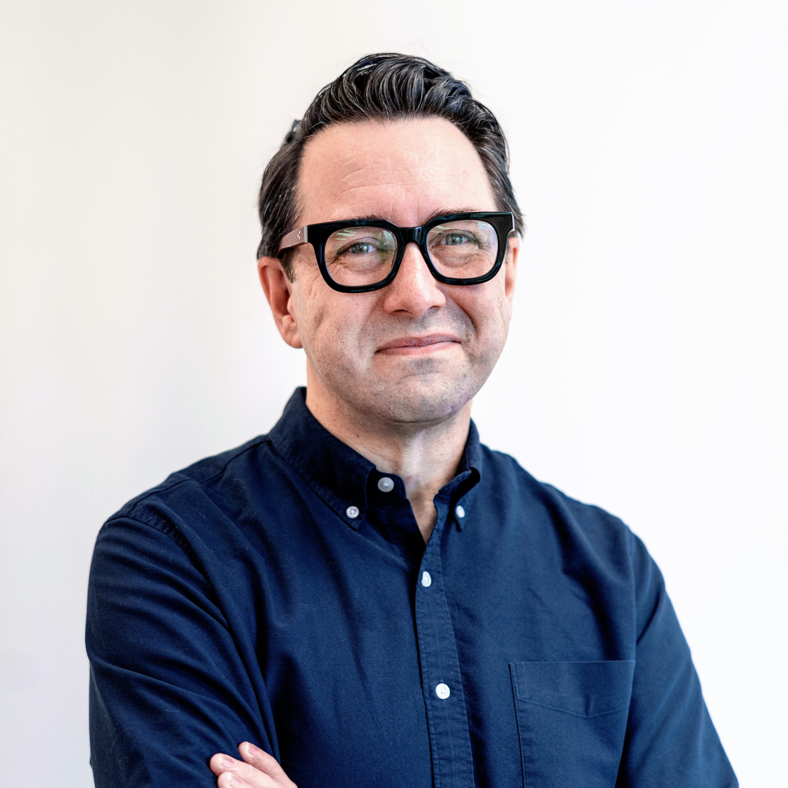 A man with dark hair and glasses wearing a blue shirt.