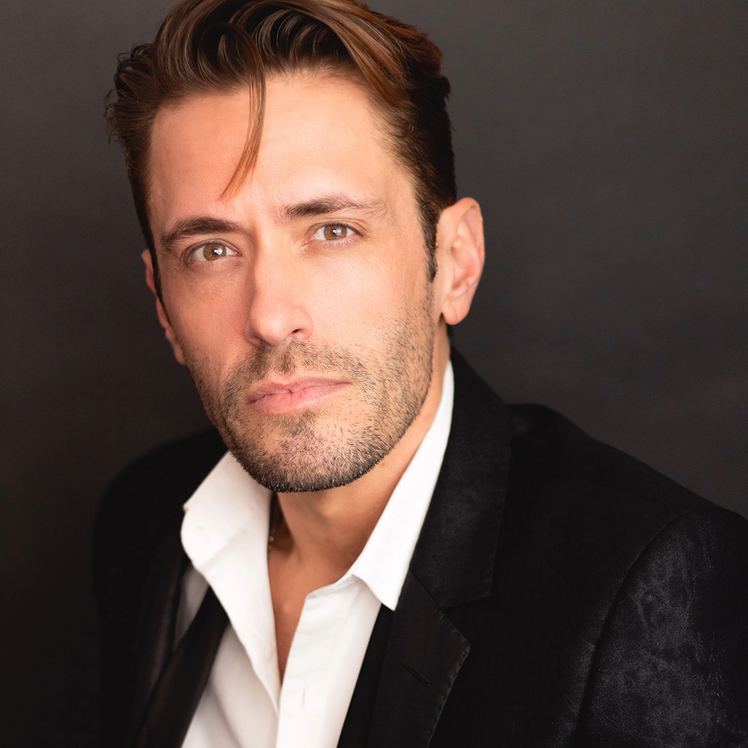 A man with brown hair wearing a white shirt and dark jacket.