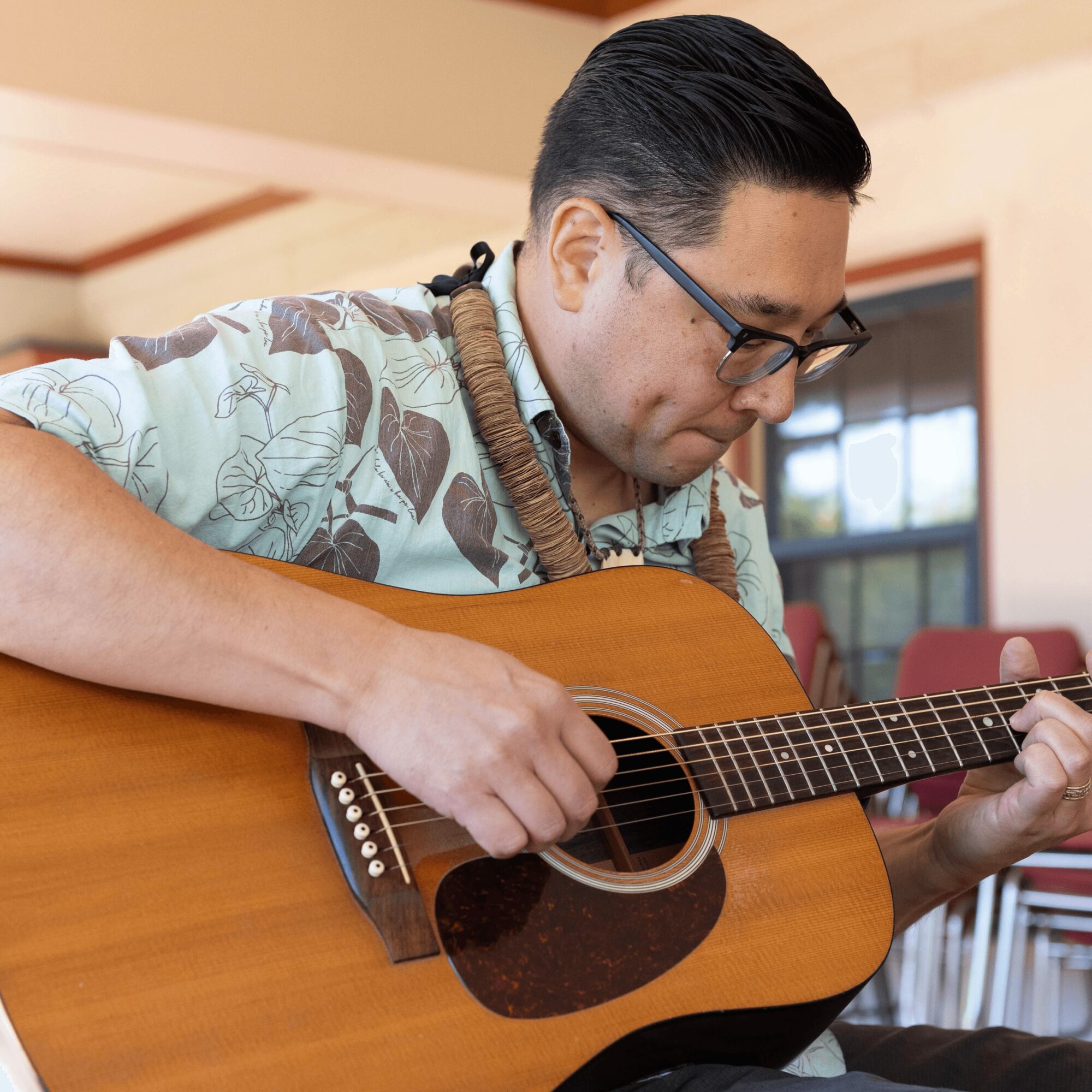 A dark-haired man wearing glasses and playing the guitar.