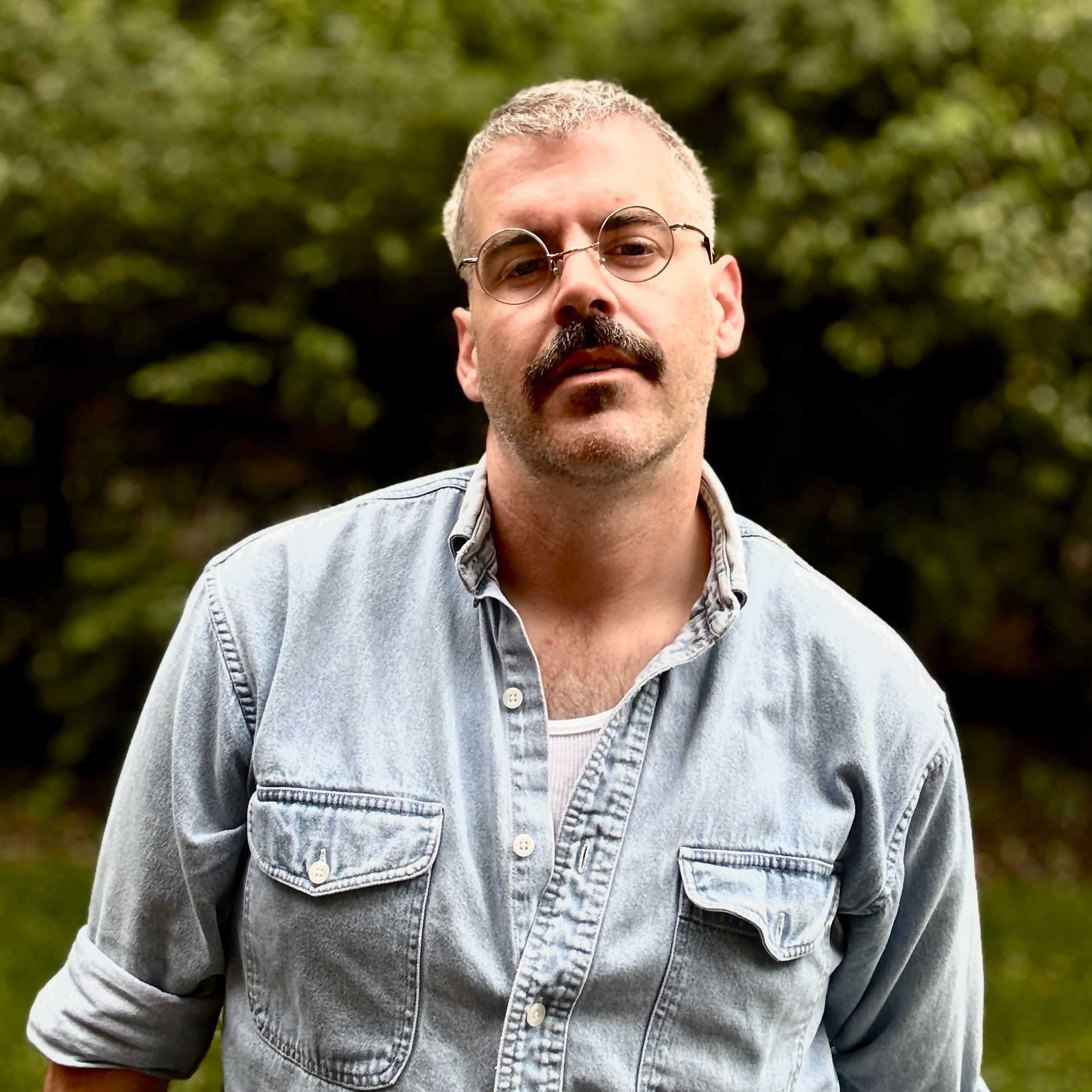 A blond man with a mustache and glasses.