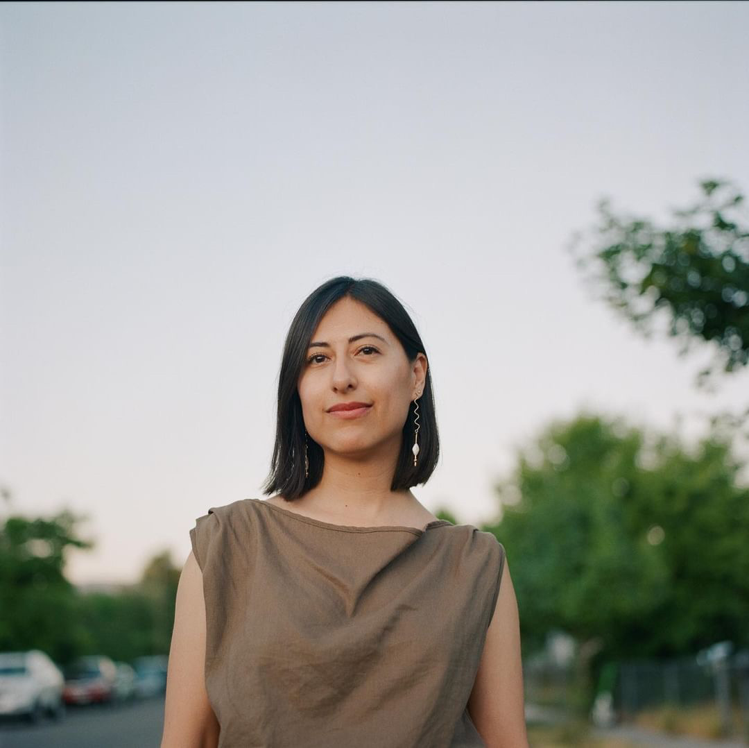 A dark-haired woman wearing a beige blouse.