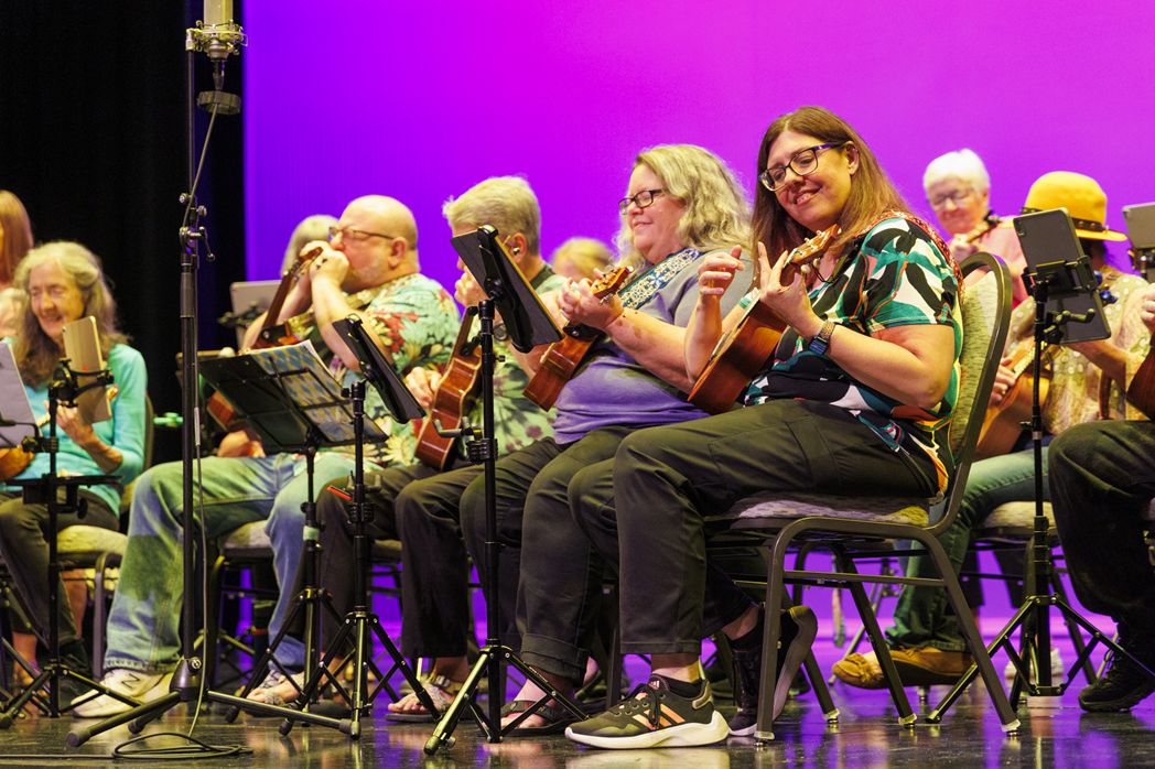 A group of people in colorful shirts plays instruments on a stage.