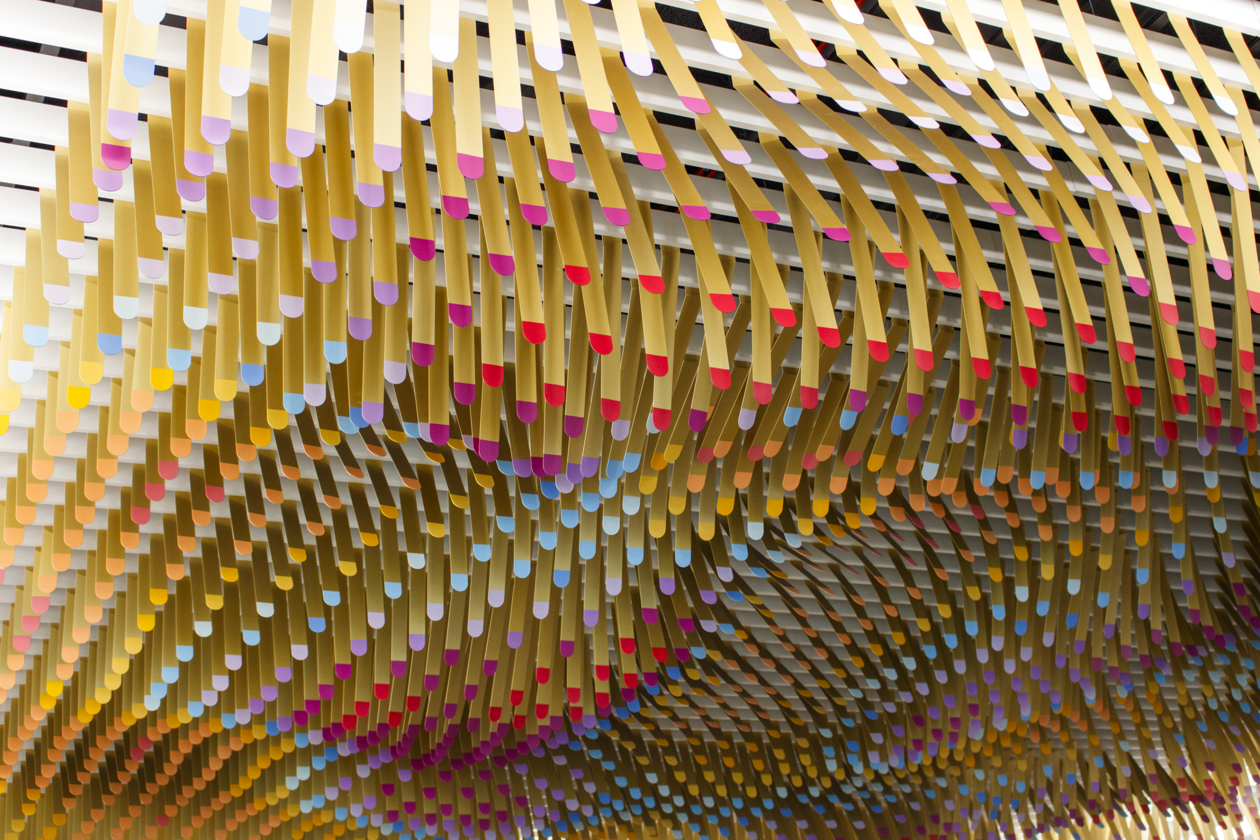 Colorful hanging rods form a wavy pattern on a ceiling, creating an abstract installation.