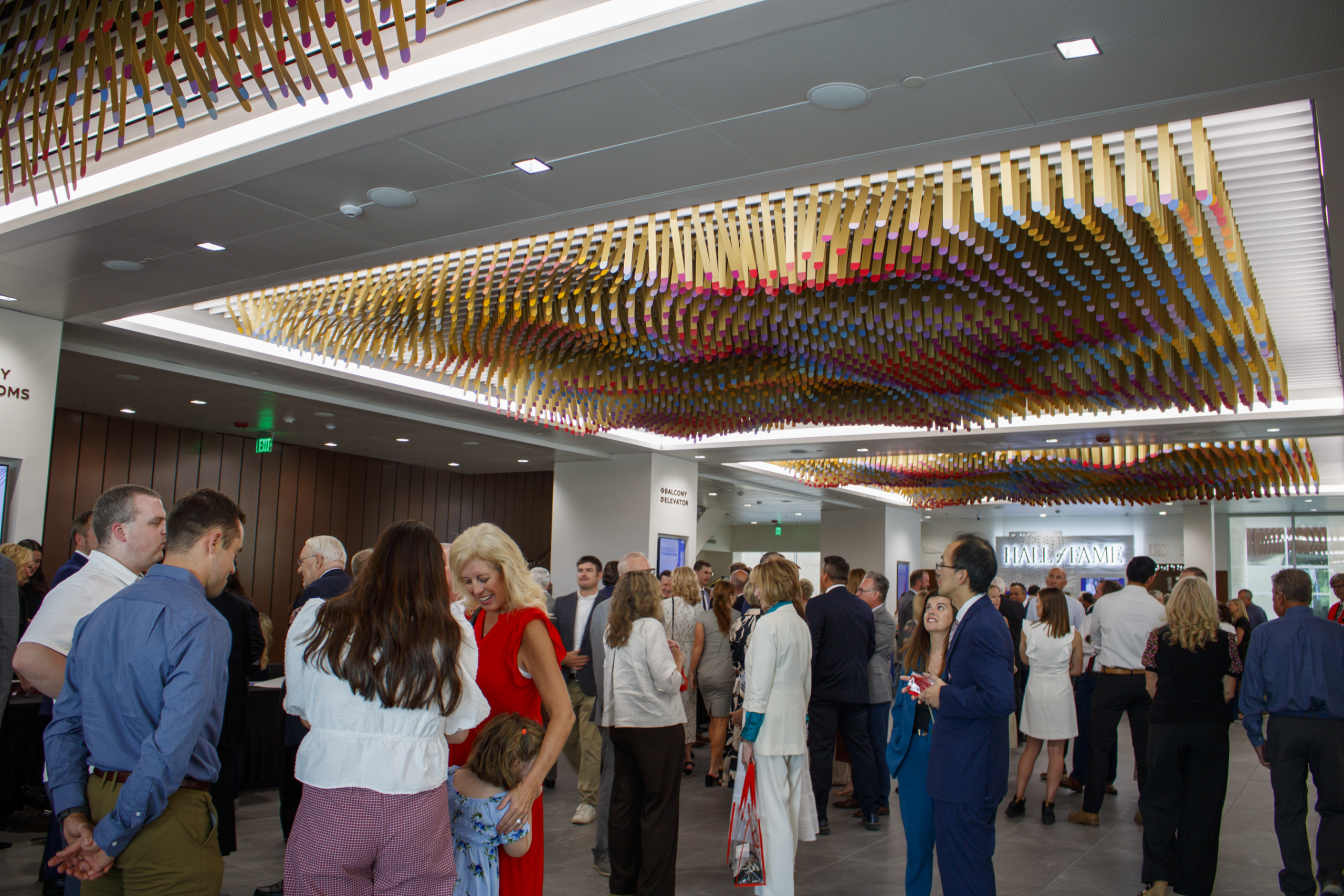 Crowd gathers in modern lobby under colorful, wavy ceiling art installation.
